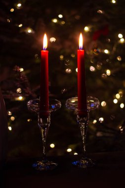 Yılbaşı ağacının arka planında, uzun cam şamdanların içinde iki kırmızı uzun mum. Romantik bir ortamda mum ışığında yeni yıl. Arkaplanda Bokeh etkisi