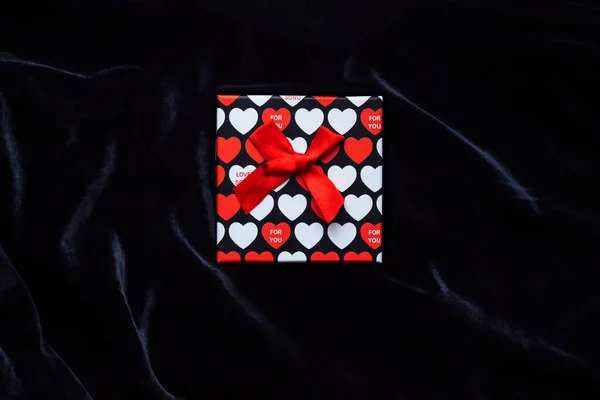 Caja de regalo con la imagen de corazones rojos para el día de San Valentín sobre un fondo de terciopelo negro. Regalo de San Valentín. Caja fuerte brillante en el centro de la foto sobre un fondo oscuro —  Fotos de Stock