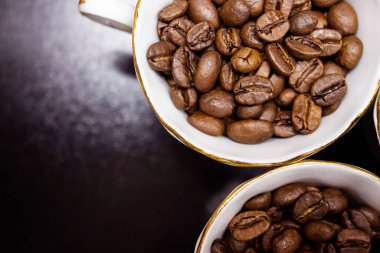 Beyaz kahve fincanındaki kahve çekirdekleri koyu bir arka planda yakın plan. Kahve çekirdekleri bir fincanın üstünde. seçici odak