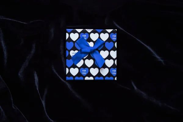 Caja de regalo con la imagen de corazones azules para el día de San Valentín sobre un fondo de terciopelo negro. Regalo de San Valentín para él. Caja fuerte brillante en el centro de la foto sobre un fondo oscuro —  Fotos de Stock