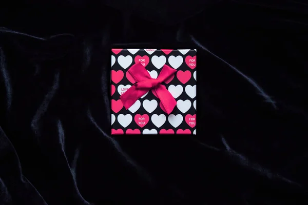Caja de regalo con la imagen de corazones en rosa para el día de San Valentín sobre un fondo de terciopelo negro. Regalo de San Valentín para ella. Caja fuerte brillante en el centro de la foto sobre un fondo oscuro —  Fotos de Stock