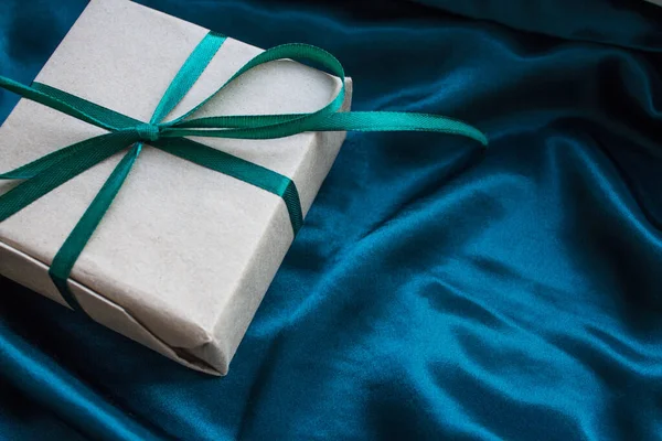 Zümrüt yeşili saten kurdeleyle sarılı bir hediye kutusu. - Mutlu yıllar. İpek zümrüt yeşili arka planda doğum günü hediyesi