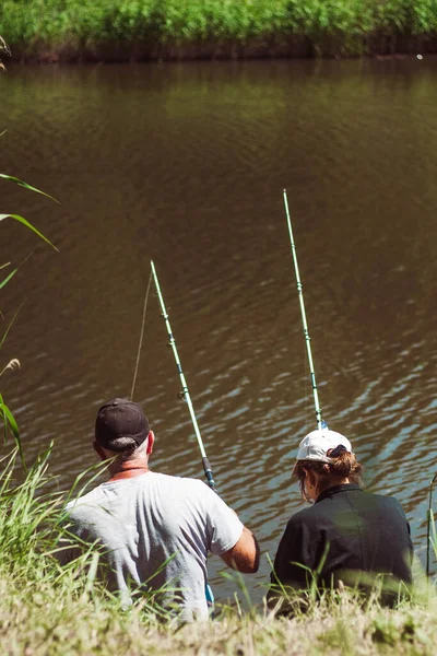 Rear view of a married couple fishing in a pond with a fishing rod. Adult couple fishing together. High quality photo