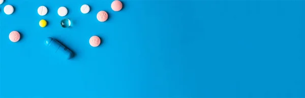 Medical banner with place for text. Pills and capsules of different colors on a blue background. The concept of medicine and health. Copy space