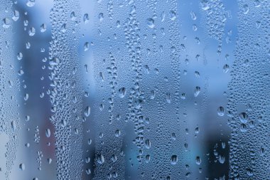 Pencere camındaki yağmur damlalarına yakın çekim. Kasvetli ıslak hava. Koyu mavi yağmur bulutlarının önünde cam üzerine su damlaları. Yağmur. Soyut arkaplan dokusu. Yüksek kalite fotoğraf