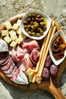 Italian snack and antipasti on a tray and red wine: prosciutto, salami, sun-dried tomatoes, olives, cheese, grissini and dates. Summer snack on the street