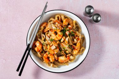 Pad thai with shrimp and peanuts on a pink background.