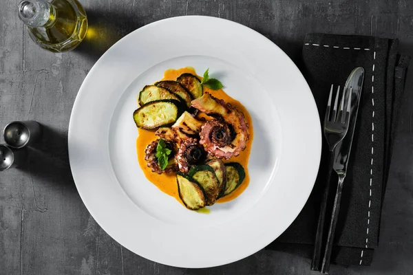cooked octopus, served with courgettes and sauce serving on the table with cutlery