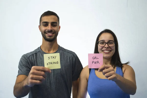 Gri gömlekli bir adam ve feminist posterli beyaz arka planda mor gömlekli bir kadın..