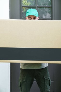 Evin kapısında duran kuryenin elinde büyük bir karton kutu vardı. Adrese teslimat var. Paketlerin taşınması ve teslimi üzerine çalışır..