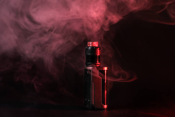 Модификация электронного Vaping устройства, распылитель стоит в дыму и паре освещаемых красным светом.