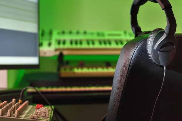 Bir müzik stüdyosundaki profesyonel kulaklıklar bulanık sentezleyicilerin ve elektronik müzik aletlerinin arka planına karşı. Kayıt stüdyosu, ses mühendisi ve yapımcının çalışma yeri.