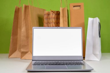White screen on a laptop against the background of paper bags with goods and purchases ordered in online market and delivered home