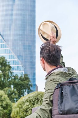 Bir ofis binasının arka planında şapkasını sallayan bir adam. Elveda el hareketi, elveda ofis ve özgürlük kavramı.