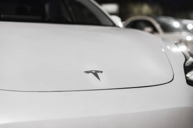 Elektrikli arabanın ön kaputunda Tesla Şirketi logosu var. Elektrikli aracın beyaz kaputunda Tesla Motors 'un amblemi Riga, Letonya - 22 Eylül 2021