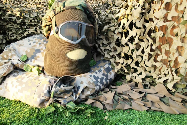 military uniforms with face shield mask, balaclava and glasses, against camouflage netting background