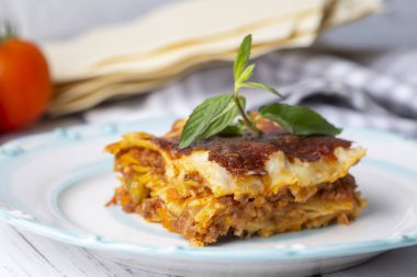 Gri bir tabakta fesleğen yaprağıyla servis edilen lezzetli bir lazanya. İtalyan mutfağı, menü, tarif. Ev yapımı et lazanyası. Yaklaş, kenar görünüm