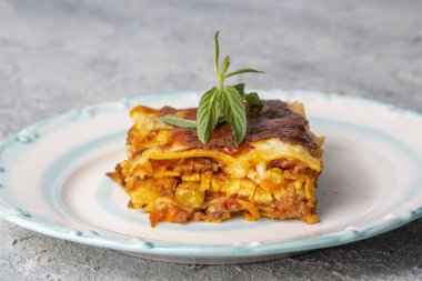 Gri bir tabakta fesleğen yaprağıyla servis edilen lezzetli bir lazanya. İtalyan mutfağı, menü, tarif. Ev yapımı et lazanyası. Yaklaş, kenar görünüm