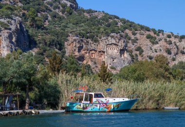 Dalyan - Mugla - Türkiye, 22 Ekim 2021, Dalyan, Mugla, Türkiye 'deki Kaunos antik kentinin kaya kesimli tapınak mezarları. Feribot ve arka planda oyulmuş mezarlarla güzel Dalyan nehir manzarası.