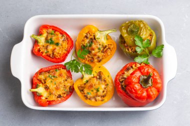 Doldurulmuş biber, pirinçle doldurulmuş yarım biber, kurutulmuş domates, otlar ve peynir mavi ahşap bir masada fırın kabında, üst manzara. Vejetaryen yemeği, doldurulmuş sebze.