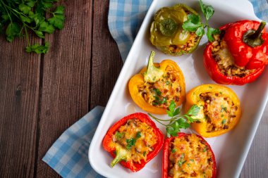Doldurulmuş biber, pirinçle doldurulmuş yarım biber, kurutulmuş domates, otlar ve peynir mavi ahşap bir masada fırın kabında, üst manzara. Vejetaryen yemeği, doldurulmuş sebze.