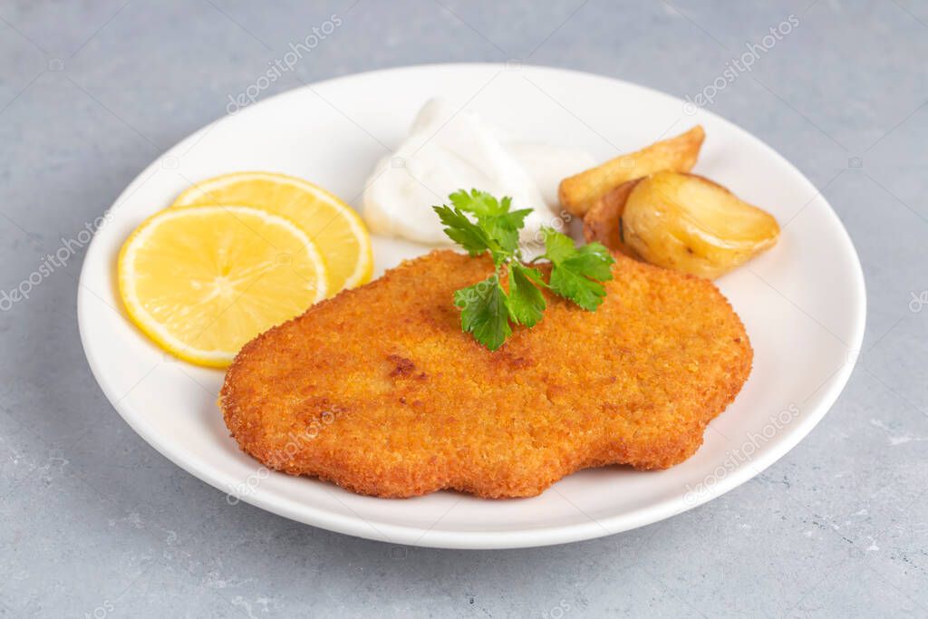 Chicken schnitzel with sauce, fried potatoes and lemon in a plate