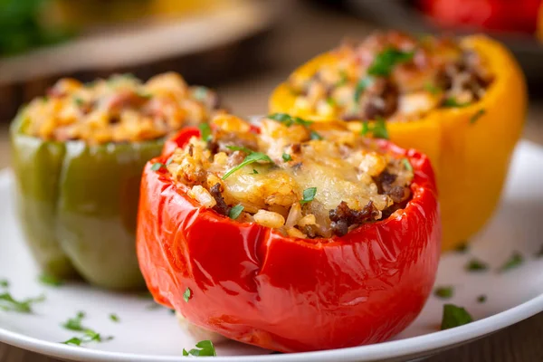 Stuffed peppers, halves of peppers stuffed with rice, dried tomatoes, herbs and cheese in a baking dish on a blue wooden table, top view. Vegetarian dish, stuffed vegetables