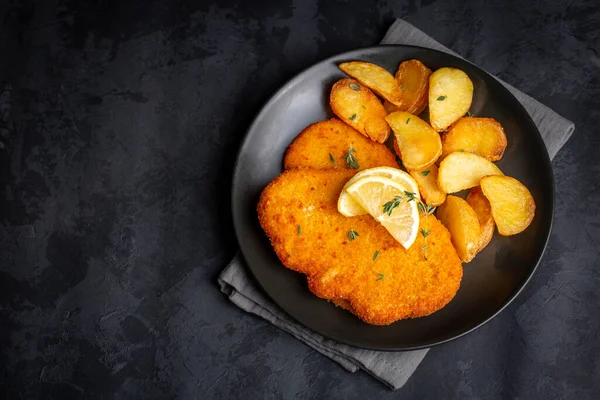 Chicken schnitzel with sauce, fried potatoes and lemon in a plate