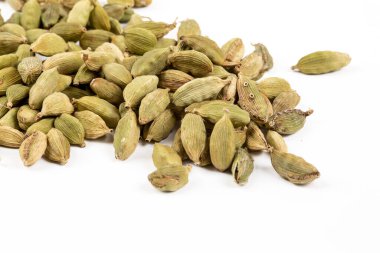 Kurumuş yeşil Elettaria kakule meyvelerinin yakından görünüşü, tohumlu kakule baharatı beyaz arkaplana saçılmış.