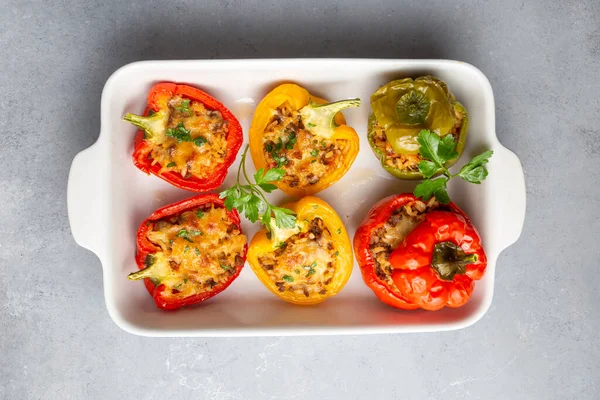 Stuffed peppers, halves of peppers stuffed with rice, dried tomatoes, herbs and cheese in a baking dish on a blue wooden table, top view. (Turkish name; biber dolmasi)