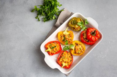Doldurulmuş biber, pirinçle doldurulmuş yarım biber, kurutulmuş domates, otlar ve peynir mavi ahşap bir masada fırın kabında, üst manzara. Vejetaryen yemeği, doldurulmuş sebze.