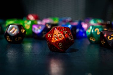 Close-up image of a red 20-sided role-playing die. In the background are various colored polyhedral dice