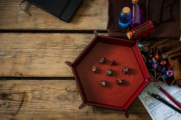 Tahta bir masanın üzerindeki TTRPG ekipmanlarıyla çevrili bir zar tepsisi..