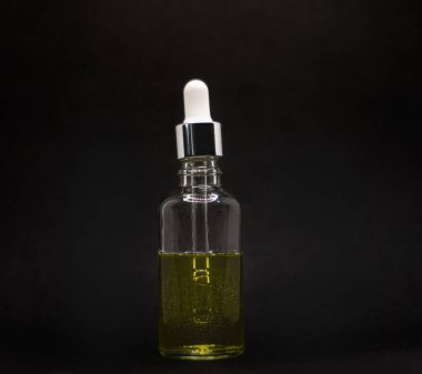 Koyu bir yüzey üzerinde altın serumu olan zarif bir şişe ve pipette. Siyah arkaplandaki yüz serumuna yakın çekim. Cilt bakımı için kolajen ve hyalürik asit.