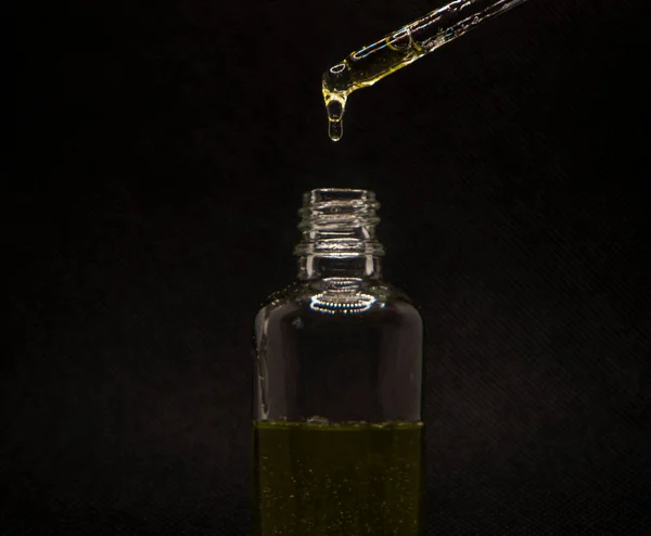 Close-up of a face serum on a black background. Collagen, hyaluronic acid for skin care. elegant bottle and pipette with golden serum on a dark surface