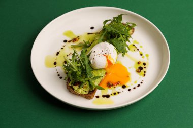 Yeşil arka planda haşlanmış yumurtalı avokado tostu, yatay.