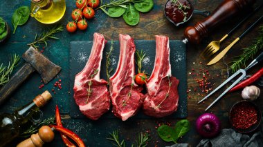 - Et. Kemiğin üzerinde biberiye ve baharatlı üç çiğ biftek. Siyah taştan bir arka planda. Üst görünüm.