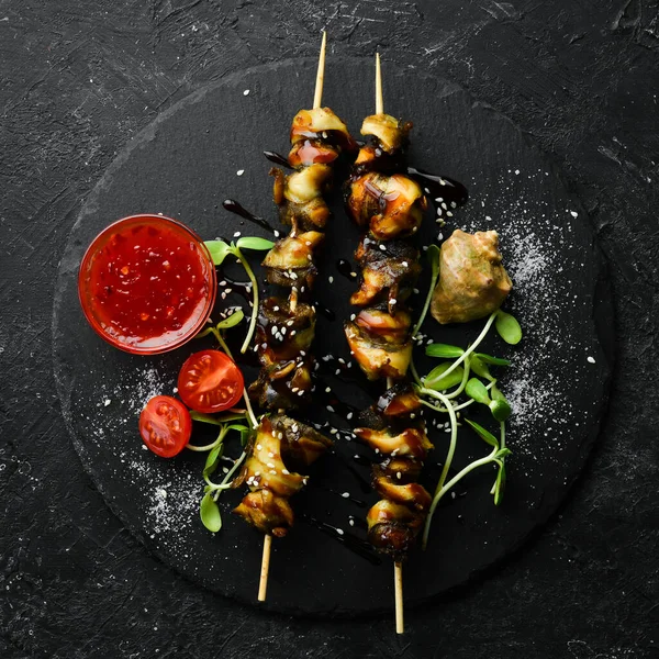 Siyah taştan bir tabakta sebzeli Rapana şişleri. Restoran yemeği. Deniz ürünleri. Kırsal tarzda. Düz Yat.