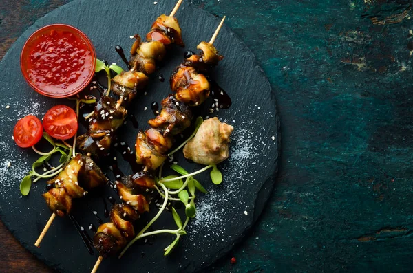 Siyah taştan bir tabakta sebzeli Rapana şişleri. Restoran yemeği. Deniz ürünleri. Kırsal tarzda. Düz Yat.