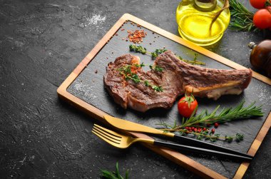 Kemiğe baharatlı dana biftek, kekik ve biberiye. Üst Manzara. Siyah taş kesme masasının üstünde düz bir görünüm vardı..