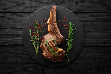 Kemiğe baharatlı dana biftek, kekik ve biberiye. Üst Manzara. Siyah taş kesme masasının üstünde düz bir görünüm vardı..