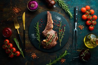 Kemiğe baharatlı dana biftek, kekik ve biberiye. Üst Manzara. Siyah taş kesme masasının üstünde düz bir görünüm vardı..
