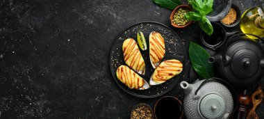 Büyük yeşil midyeler, sarımsak soslu peynirle pişirilmiş siyah taş tabakta. Üst görünüm.