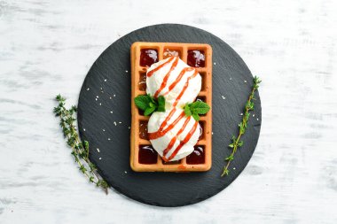 Belçika waffle 'ı: dondurma, çilek reçeli ve naneli. Tatlı. Siyah taştan bir tabakta.