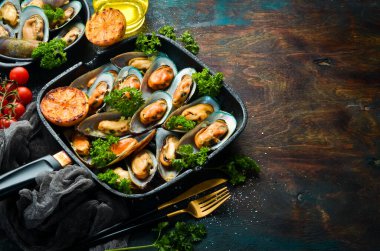 Kızarmış midye, sarımsak, maydanoz, limon ve baharatlı tava. Siyah taştan bir arka planda. Metin için boş alan.