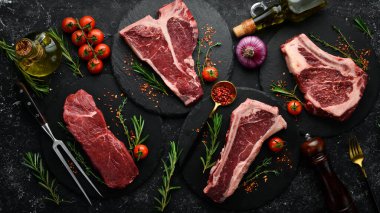 Meat. Set of raw steaks - t-bone, tomahawk, striploin, tenderloin, new york steak. Flat lay top view on black stone cutting table. clipart
