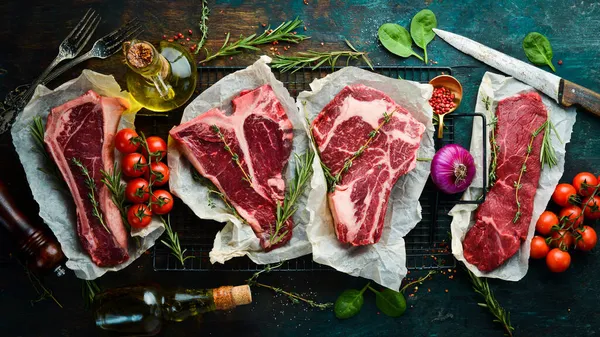 - Et. Çiğ biftek seti - T-bone, tomahawk, striploin, fileto, New York bifteği. Siyah taş kesme masasının üstünde düz bir görünüm vardı..