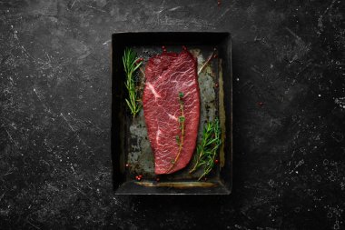 - Et. Biberiye ve baharatlı çiğ dana biftek. Siyah taştan bir arka planda. Üst görünüm.