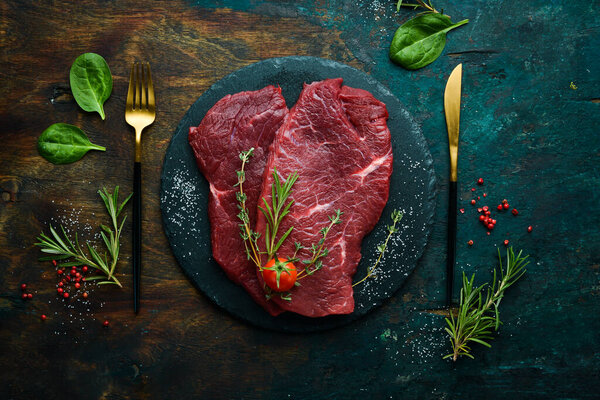 Meat. Raw veal steak with rosemary and spices. On a black stone background. Top view.