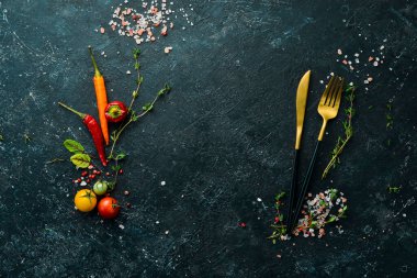 Sebze ve baharatlı siyah taş bir masanın üzerindeki çatal bıçak takımı. Yemek arkaplanı. Üst Manzara. Kırsal biçim.